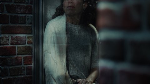 Hispanic Female in Melancholic Mood, Runs her Finger across Rainy Windoy Glass and Thinking About Life Problems. Portrait of a Troubled Lonely Woman. Mental Health, Domestic Abuse concept