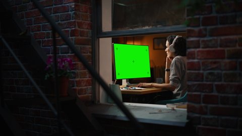 Female Designer Using Desktop Computer with Green Screen Chroma Key Monitor. Remote Access Manager Listening to Music or Podcast in Headphones, Freelancer Working at Night. Zoom Out Window Shot