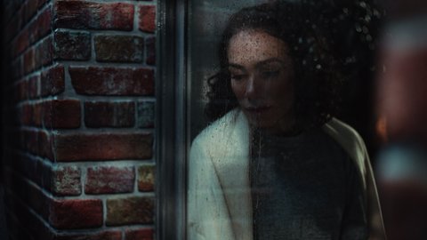 Depressed Woman Suffering from Domestic Violence Looks out of Window. Lonely Depressed Woman Suffering Silently. Mental Health Problems Concept. Inside Apartment Rainy Window Shot