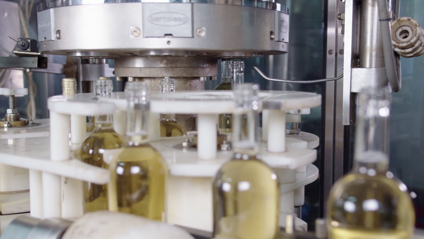 Wine production factory. Glass bottles filled up with white wine Bottling production line.