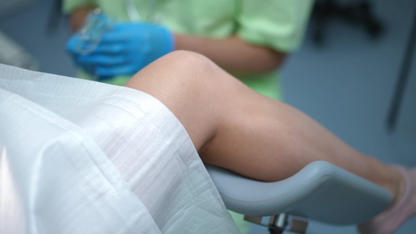Close-up leg of woman lying on gynecological chair with blurred doctor using vaginal speculum at background. Expert obstetrician examining Caucasian young patient in hospital | Shutterstock HD Video #1091297401