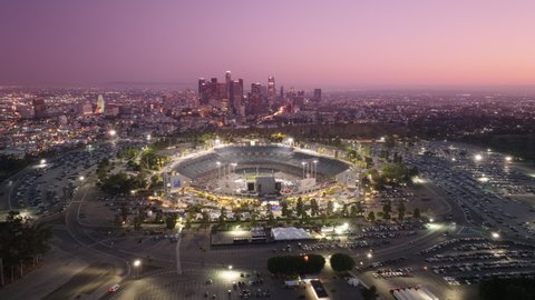 Drone flying above Dodgers stadium illuminated at night on cinematic evening. Epic downtown view on pink cinematic sunset. Skyscraper buildings, Sport game at Dodgers Stadium Los Angeles USA June 2022