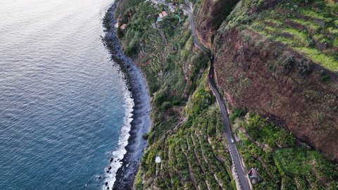 Cars drive scary cliffside road under cascading Anjos waterfall, Madeira; aerial