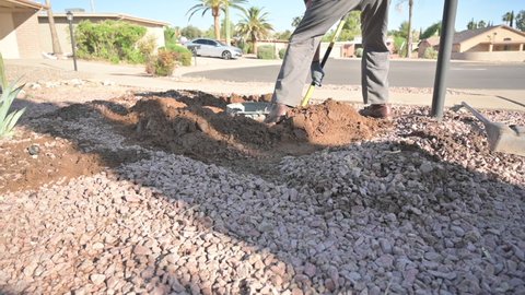 Man shoveling heavy clay sand to dig out an underground trash can, slow motion. Low angle view.