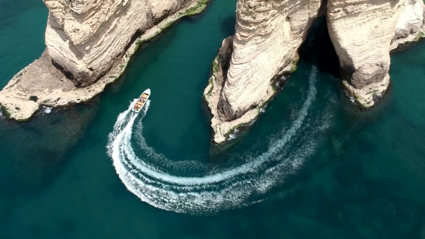 Overhead Shot Of Small Boat Passing Between Two Huge Pigeon Rocks In Rawshe Coastline, Beirut City , Lebanon Royalty-Free Stock Footage #1091303209