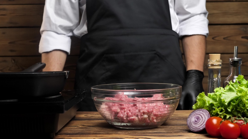 Close-up of male hands in black gloves of an unrecognizable chef mixing fresh ground beef in a glass bowl