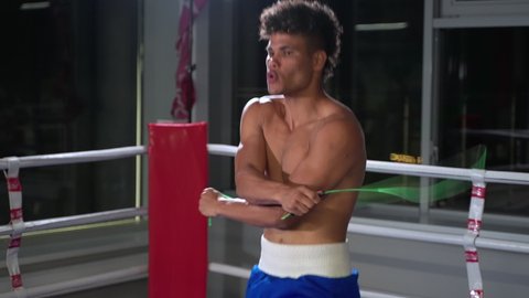 Slow motion shot of a young athletic Hispanic boxer skipping a rope in the boxing gym. Warming up with cardio before training