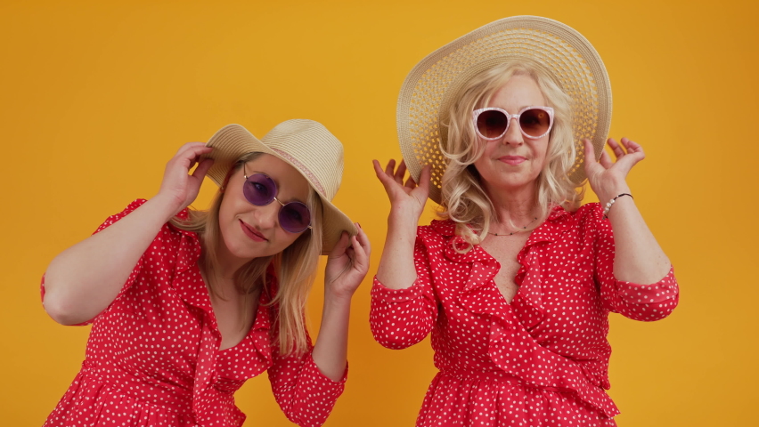 two beautiful women posing with hats and sunglasses medium shot studio shot orange background summer concept. High quality 4k footage