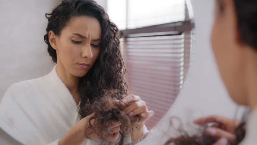 Upset sad young woman distressed by damaged hair frustrated about split ends girl worried about loss brittle dry hair hormone problem vitamin deficiency reflecting in mirror haircare treatment concept Royalty-Free Stock Footage #1091310993