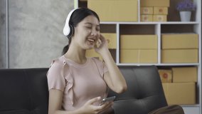 A young Asian woman wearing headphones can happily listen to music on a sofa at home.