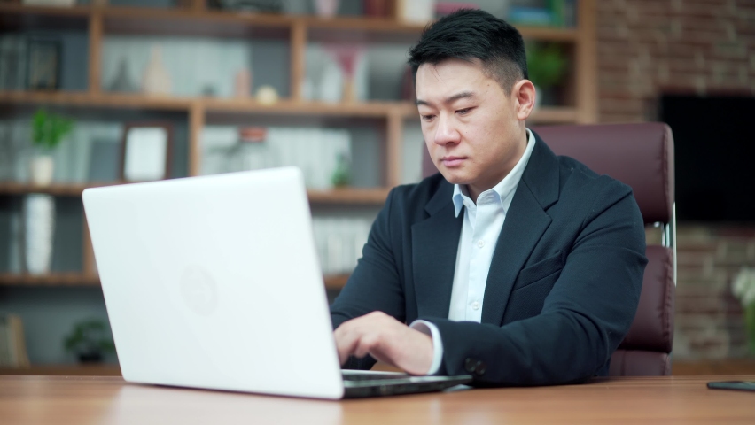 Portrait thoughtful asian male businessman working on pc laptop computer at modern office desk Confident Focused pensive business man employee in suit indoor. thinking of inspiration solving a problem | Shutterstock HD Video #1091314523