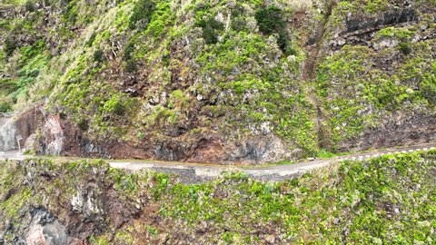 Scenic coastal cliffside road carved into steep mountain slope; Madeira aerial