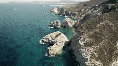 Slowly moving past a rocky cliffside overlooking the breathtaking turquoise blue water of the Mediterranean. Summertime Milos Greece 4k.