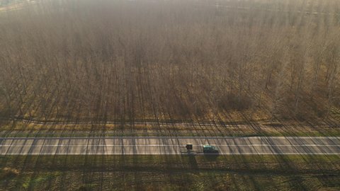 Green multi-purpose vehicle car with trailer on highway through wooded landscape, aerial view from drone pov