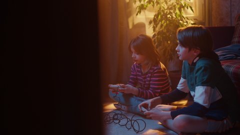 Nostalgic Childhood Concept: Young Brother and Sister Playing Old-School Arcade Video Game on a Retro TV Set at Home in a Room with Period-Correct Interior. Friends Win the Level and High Five.