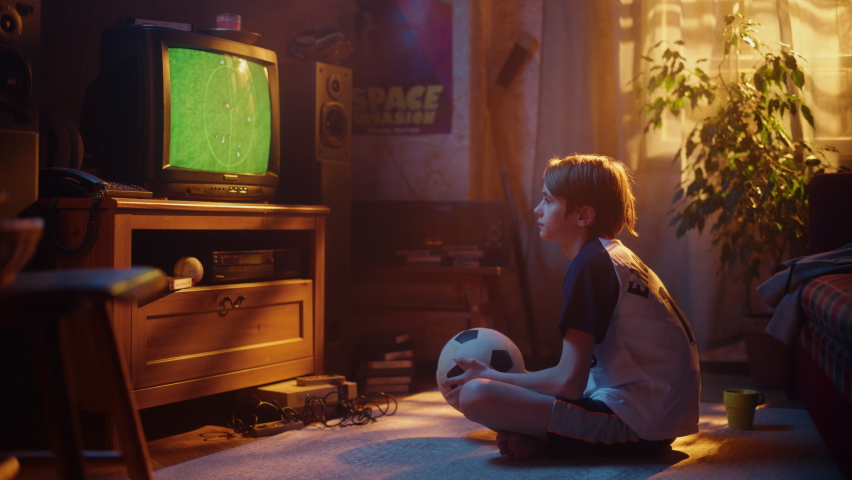 Young Sports Fan Watches a Soccer Match on Retro TV in His Room with Dated Interior. Boy Supporting His Favorite Football Team, Feeling Proud When Players Score a Goal. Nostalgic Childhood Concept. Royalty-Free Stock Footage #1091320885