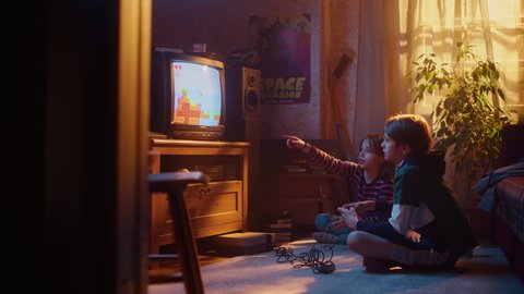 Nostalgic Childhood Concept: Young Brother and Sister Playing Old-School Arcade Video Game on a Retro TV Set at Home in a Room with Period-Correct Interior. Friends Pass the Level and Win.