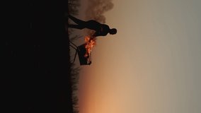 A man rolls a burning cart from a supermarket in an empty field, against the background of a golden sunset closer to the dark night, A basket of goods is lit outdoors on Black Friday, vertical video