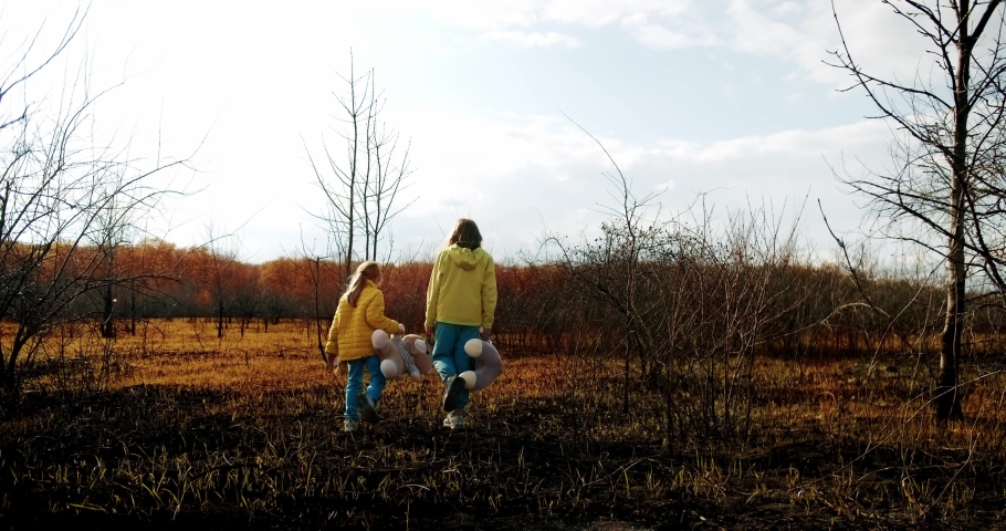 Ukrainian girls childs holding fluffy bears in clothes in the colors of the Ukrainian flag on earth destroyed and burned. Crisis, peace, stop aggression. Ukrainian national colors, Sad refugee.