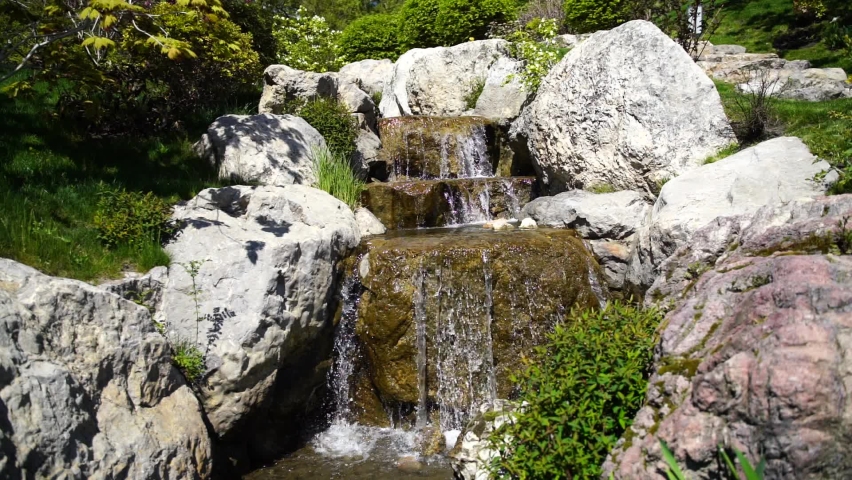 Waterfall in a Japanese garden, water slowly flows over large stones of volcanic origin