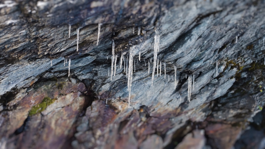 Thin fragile icicles hang from the stone ceiling. Slow-motion, pan right.