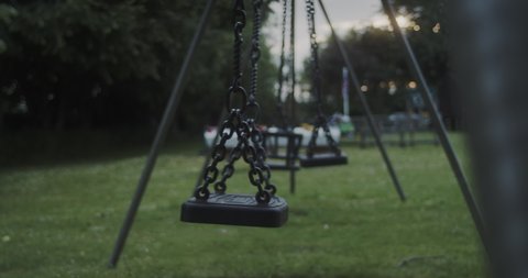 Empty swing moving at a playground in a rural countryside village, at dusk. HANDHELD, SLOW MOTION.