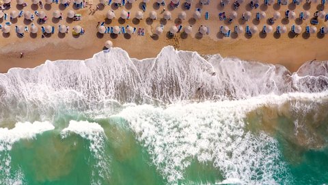Aerial view of the sea, sandy beach, sun umbrellas and sunbeds, unrecognizable people. Beautiful vacation and tourism destination in Crete, Greece.
