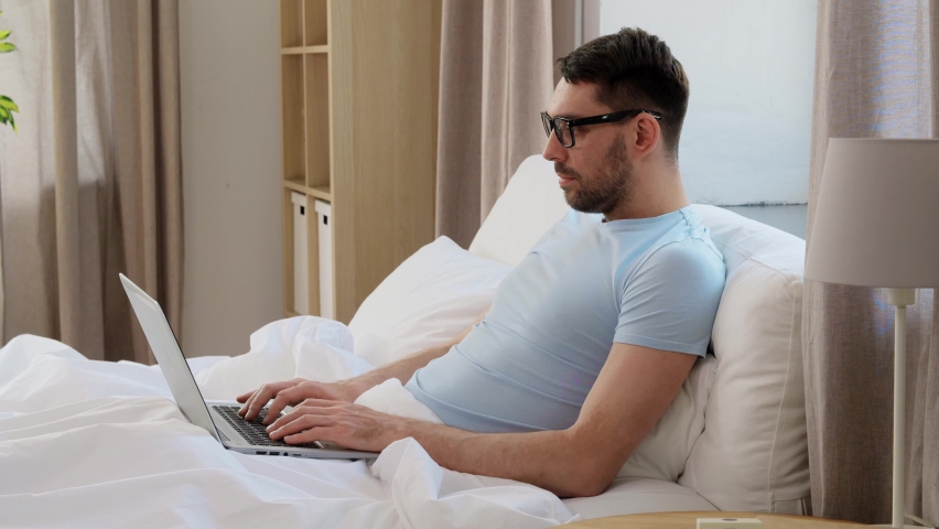 People, technology and remote job concept - man in glasses with laptop computer getting out from bed at home bedroom | Shutterstock HD Video #1091333525