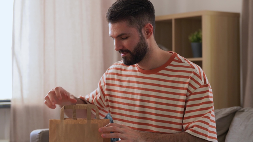 Consumption, eating and people concept - smiling man unpacking takeaway food in paper bag at home | Shutterstock HD Video #1091333589