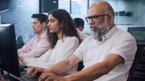 An elderly or old Indian Asian man or male wearing eyeglasses or spectacles sitting in front of the computer with office colleagues or employees busy working together. Healthy work environment concept - Powered by Shutterstock - Get 15% off with code: PIKWIZARD15