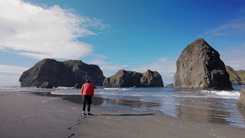 Adult man enjoying beautiful panoramic ocean views. Active traveler wandering sandy beach surrounded by rocky formations along the shoreline. High quality 4k footage