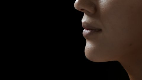 Big close-up shot of young pretty African American woman strokes her lips on black background | Dry lips prevention concept