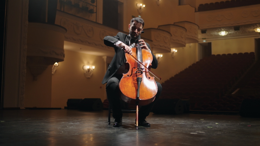 cellist is playing violoncello on scene in empty old opera house, rehearsal of symphonic orchestra