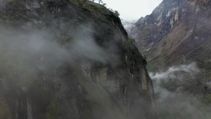 Epic aerial rotating shot of a foggy cliffside inside a valley of the Annapurna mountains, Nepal