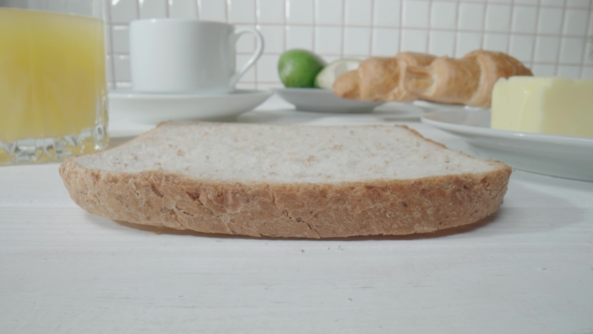 A spoon pouring raspberry jam onto a piece of bread toast. Close up of a sandwich with sweet jam. Cooking delicious breakfast in the morning in the kitchen. Sweet dessert, yummy, fast food.