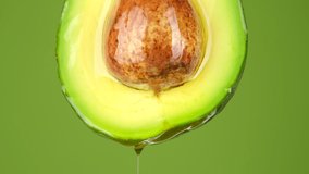 fresh organic green avocado fruit with oil stream, isolated on green background