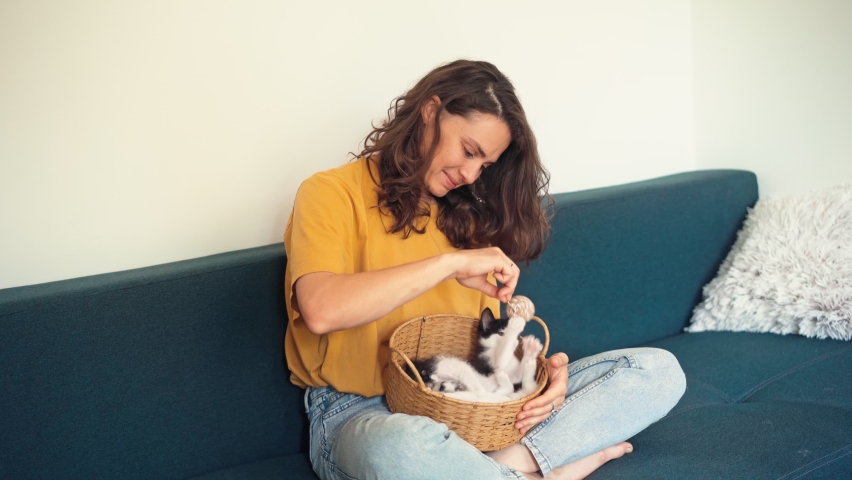 A young woman plays with her two cute kittens while sitting on the couch