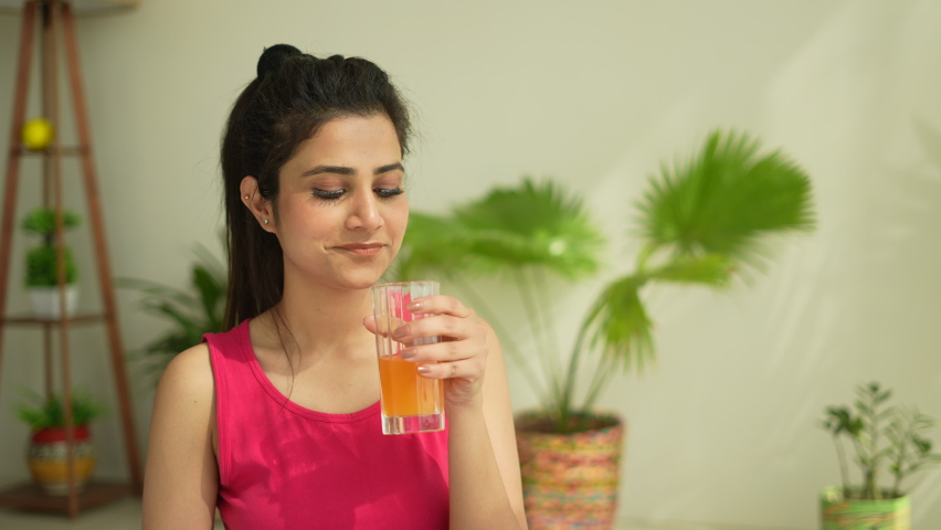Pretty Indian young woman drinking healthy juice and smiling after doing yoga in morning.Asian female doing yoga and drink orange juice.healthy concept.female fitness.