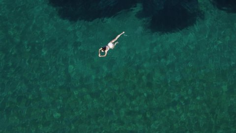 Top view of young female in white swimsuit floating on water surface in crystal clear turquoise ocean. Happy island lifestyle. Aerial drone view. Vacation , relax, travel