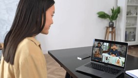 Video meeting, online conference with multiracial coworkers. Young Asian woman is using laptop app for video communication with several diverse people together while sitting at the table at home