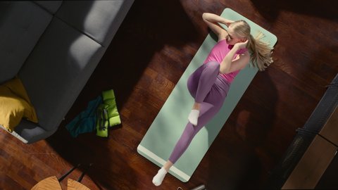 Top View Sport: Gorgeous Girl Doing ABS Elbow to Knee Crunches Lying on an Exericise Mat at Home. Fit, Authentically Beautiful Young Woman Does Workout in Her Apartment. Overhead Zoom out Shot