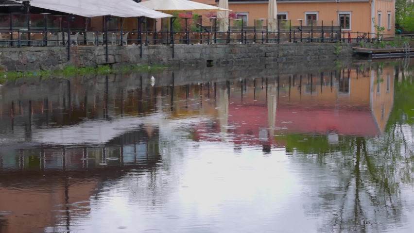 Beautiful view from outdoor restaurant on river coast to it's reflection on water and increasing stream. Europe. Sweden. Uppsala.  | Shutterstock HD Video #1091360753