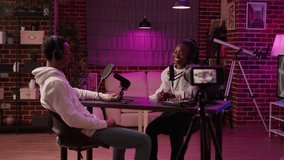 African american couple recording vlog using digital camera while recording podcast using professional microphone and audio equipment. Content creator interviewing famous vlogger in home studio.