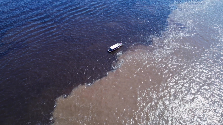 Boat sailing at Meeting of the Waters tourism landmark at Manaus Amazonas Brazil. Brown Amazon river side Black Negro River with two different colors. Amazon rainforest Brazil. Manaus Amazonas Brazil.