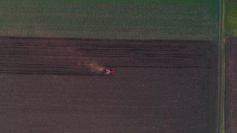 Agricultural tractor with tiller attached performing soil tillage in field, aerial view from drone pov