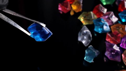 Trinket gems laying on black surface, professional carefully examines the fake