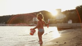 Slow motion video of a little girl running on the beach at sunset. Beautiful baby rejoices by the ocean on vacation. High quality 4k footage