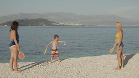 Slow motion video of a family playing tennis on the beach by the ocean. Active sports on leisure pastime together with children.
