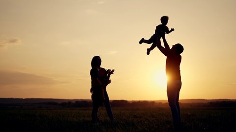Happy family. Family picnic on green grass. Parents play with children in park. The father lifts baby up. Happy family concept. Family game in park. Children dream. Silhouette of people in the park