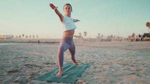 Full length shot of beautiful girl doing yoga on fitness mat on the beach. Attractive woman in sportswear doing stretching workout during yoga class outdoors